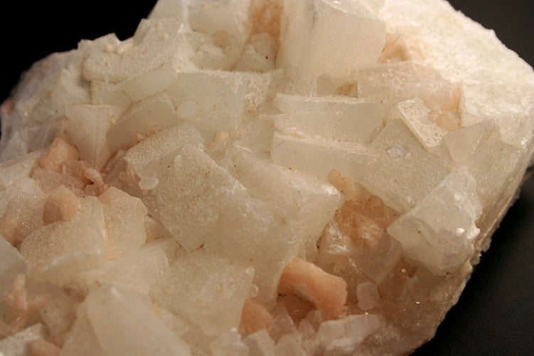 A close-up of a white and pale peach crystal cluster with sharp cuboid and blocky mineral formations on a dark background.